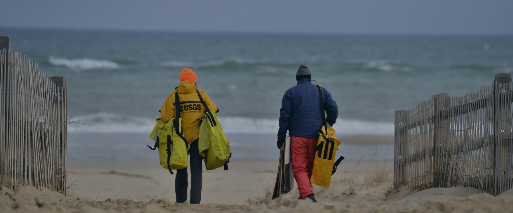 Two scientists carry equipment out to the seashore.